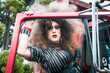 drag queen with big wig standing at an old car