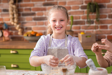 Happy smiling cute girls at the kitchen island take the kitchen apron and preparing the dough the delicious biscuits they spending wonderful time together