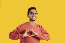 Headshot picture of smiling young black man isolated on yellow studio background show heart hand gesture. Portrait of happy African American guy demonstrate love sign share affection and care.