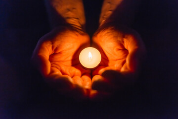 Wall Mural - Burning candle in a mans hand religion concept.Candle in hands on a dark background.