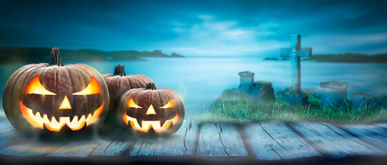 Wall Mural - three spooky halloween pumpkin, jack o lantern, with an evil face and eyes on a rustic wooden bench,