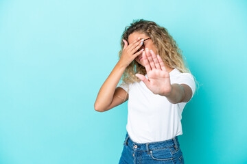 Wall Mural - Girl with curly hair isolated on blue background making stop gesture and covering face