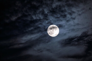 full moon at night. the illuminated face of the moon is wrapped in a cloud cover that covers it in a