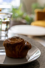 pancake or cupcake on ceramic plate, terrazzo table, in the background out of focus armchairs and glass of water