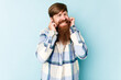 © Asier - Young caucasian red-haired man isolated on blue background covering ears with hands.