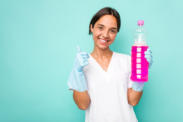 Wall Mural - Young cleaner hispanic woman isolated on blue background smiling and raising thumb up