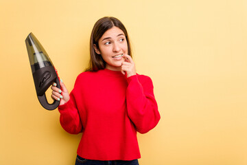 Wall Mural - Young caucasian woman holding a hand vacuum cleaner isolated on yellow background relaxed thinking about something looking at a copy space.