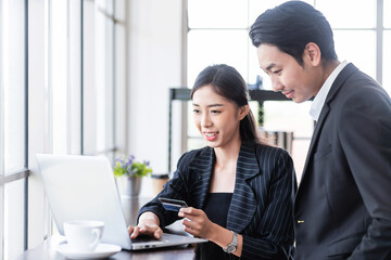 Two Asian business people use a credit card for online payments. Business people shop online, e-commerce, internet banking and spend money with security and confidence.