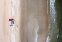 Aerial View Top Down Of Four Wheel Drive Vehicles On The Beach Near The Ocean With A Tent On The Sand