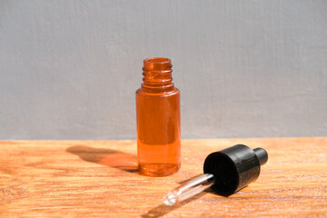 orange bottle with skin oil stands next to pipette on wooden surface against gray wall