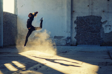 Wall Mural - Ballerina jumping and dancing in a dusty abandoned building on a sunny day