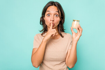 Wall Mural - Young hispanic woman holding yogurt isolated on blue background keeping a secret or asking for silence.