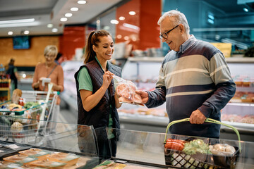 Wall Mural - Happy supermarket manager assists senior man in choosing meat packages.