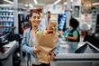 © Drazen - Happy woman with paper bag full of groceries in supermarket.