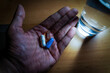 A hand with vitamins minerals and omega 3 supplement capsules next to a glass of water. A male person having health vitamin supplements displaying healthy lifestyle.