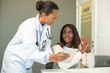 © KAMPUS - Smiling doctor consulting woman showing digital tablet to her. Young African American female patient sitting at doctors office and listening to general practitioner. Medical consultation concept