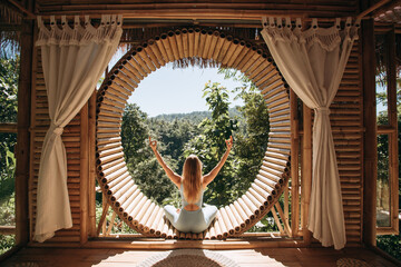 Wall Mural - An attractive slim woman practices yoga in a bamboo house in Bali. The concept of fitness, sport, training and lifestyle. Yoga in a beautiful place.