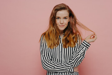 Young playful woman dressed in casual clothes playing with hair