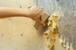 a young man cleans the wall of old wallpaper with a spatula. handyman preparing the wall for new wallpaper