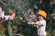 © Юлия Клюева - A little boy is playing with a garden hose in the backyard on a hot sunny day. A preschool child is watering flowers in the garden. The concept of raising a child and teaching him to work.