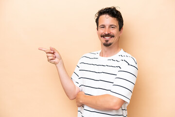 Young caucasian man isolated on beige background pointing finger to the side