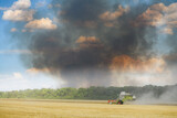Fototapeta  - Combine harvester against the backdrop of black smoke rising into the sky.