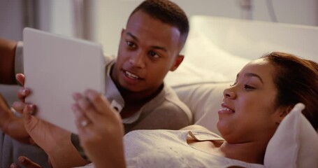 Wall Mural - Couple browsing on a tablet, talking and watching movies or series online together on the couch at home. Happy husband and wife relaxing, streaming videos and bonding while lying in bed