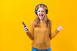 Woman dancing to music while listening to MP3 player with wired headphones. Energy move of caucasian dancer isolated on yellow background. Happy girl rejoices at free time in the studio