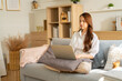 © Yingyaipumi - Bussy Asian freelance business women casual wear sitting on sofa using laptop looking at screen typing message,working call video conference in living room.Happy young girl working at home in summer