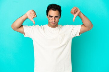 Wall Mural - Caucasian handsome man over isolated blue background showing thumb down with two hands