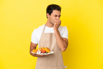 Wall Mural - Restaurant waiter holding waffles over isolated yellow background having doubts