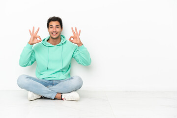 Wall Mural - Caucasian handsome man sitting on the floor showing an ok sign with fingers