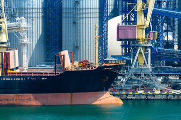 Wall Mural - industrial infrastructure of seaport, sea, cranes and dry cargo ship, grain silo, bulk carrier vessel and grain storage elevators, concept of sea cargo transportation