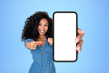 African woman pointing at large phone with blank screen, blue background