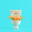 Orange lily flower with green leaves in beige toilet on isolated vivid turquoise-blue background. Minimal spring or summer floral, optimistic, hopefulness concept. The idea of the bright side of life.