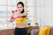 © khwanchai - Asian beautiful woman in sport wear exercise and work out at home with dumbbells.