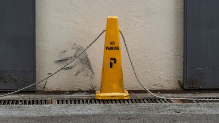 close-up yellow cone bounding the area of the parking space for cars against a white wall. Traffic control tools.