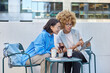 © wayhome.studio  - Female multiracial coworkers use touch pad work on startup project together watch training webinar sit at small table in outdoor cafe drink cocktail make journalistic research using modern technology