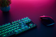 High Angle View Of Backlighted Keyboard And Mouse Laying On Desk. Purple Light From Top.