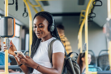 Poster - African american woman riding a bus and using a smartphone and headphones