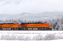 Two Freight Trains, With Three Locomotives Visible, Pulling Cargo Through A Mountainous Region Close To Whitefish, Montana In Winter
