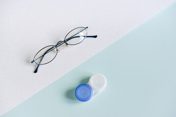 Glasses and a case for contact lenses on a white and blue background. concept of choosing a method of vision correction. copy space