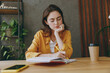 © ViDi Studio - Young smiling happy cheerful fun european successful employee business woman 20s she wearing casual yellow shirt writing in notebook diary sit work at wooden office desk Achievement career concept