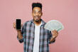 © ViDi Studio - Young man of African American ethnicity in blue shirt hold use mobile cell phone with blank screen workspace area fan of cash money in dollar banknotes isolated on plain pastel light pink background