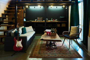 Part of garage or room inside house with bottles of beer, cups and square boxes on table standing between couch with cushions and armchair