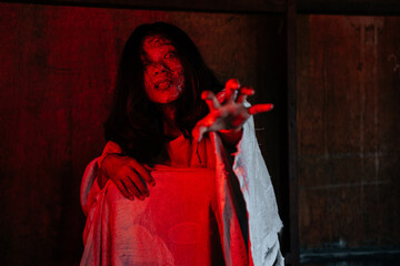 Asian woman dressed in white and put on a blood-stained face in a dark deserted area reflected by red light.