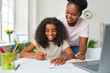 © Studio Romantic - Help with homework. Joyful african american teenage girl doing school homework at home with mom's help. Smiling young dark-skinned woman watches her daughter write in notebook. Education and family.