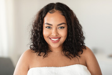 Beauty portrait of african american oversize lady standing wrapped in towel and smiling at camera