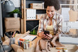 © lordn - Young African-American entrepreneur woman working in her small workshop using smartphone. Online banking apps for entrepreneurs