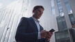© stockbusters - Successful businessman using smartphone going in downtown district close up.